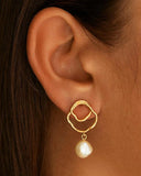 Gold plated abstract circle earrings with dangling natural pearl, combining artistic design with timeless elegance — επιχρυσωμένα σκουλαρίκια με αφηρημένο κυκλικό σχέδιο και κρεμαστό φυσικό μαργαριτάρι, που συνδυάζουν μοντέρνα αισθητική και διαχρονική κομψότητα. Διαθέσιμα στο Iconic Angels Glyfada.