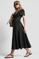 Black midi cotton dress with deep V-neckline, short wide sleeves and structured waist with double buckle belt detail, combining feminine silhouette with modern edge — μαύρο midi φόρεμα με V ντεκολτέ, κοντά φαρδιά μανίκια και ζώνη με διπλή αγκράφα στη μέση, ιδανικό για elegant day to night looks. Διαθέσιμο στο Iconic Angels Glyfada.