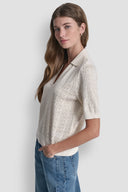 Cream short-sleeve knit polo top with subtle all-over DKNY monogram pattern, V-neckline and structured collar, blending elevated minimal style with everyday comfort — εκρού πλεκτό polo top με διακριτικό DKNY monogram, V ντεκολτέ και γιακά, ιδανικό για chic casual και smart day looks. Διαθέσιμο στο Iconic Angels Glyfada.