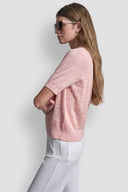 Pink short-sleeve knit polo top with subtle all-over DKNY monogram pattern, V-neckline and classic collar, combining feminine elegance with modern minimal style — ροζ πλεκτό polo top με διακριτικό DKNY monogram, V ντεκολτέ και γιακά, ιδανικό για chic casual και polished day looks. Διαθέσιμο στο Iconic Angels Glyfada.