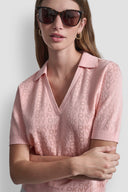 Pink short-sleeve knit polo top with subtle all-over DKNY monogram pattern, V-neckline and classic collar, combining feminine elegance with modern minimal style — ροζ πλεκτό polo top με διακριτικό DKNY monogram, V ντεκολτέ και γιακά, ιδανικό για chic casual και polished day looks. Διαθέσιμο στο Iconic Angels Glyfada.