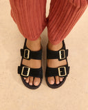 Suede Nordic sandals in classic black with satin gold buckles and a natural jute footbed, combining timeless elegance with everyday comfort — μαύρα suede Nordic σανδάλια με σατινέ χρυσές αγκράφες και φυσικό πάτο από σχοινί, ιδανικά για effortless chic εμφανίσεις που φοριούνται από το πρωί έως το βράδυ. Διαθέσιμα στο Iconic Angels Glyfada.