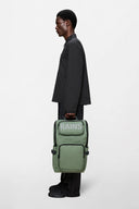 Cargo-style green backpack with bold RAINS logo, multiple zip compartments and structured silhouette, functional and modern for everyday use or travel — πράσινο backpack cargo με έντονο λογότυπο RAINS, πολλαπλές θήκες με φερμουάρ και δομημένο σχήμα, πρακτικό και σύγχρονο για καθημερινές εμφανίσεις ή ταξίδια. Διαθέσιμο στο Iconic Angels Glyfada.