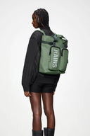 Waterproof green backpack with bold RAINS logo, structured design and practical front pockets for everyday essentials — αδιάβροχο πράσινο backpack με statement λογότυπο RAINS, minimal αισθητική και λειτουργικές μπροστινές θήκες για άνετη οργάνωση στην πόλη ή στις αποδράσεις του weekend. Διαθέσιμο στο Iconic Angels Glyfada.