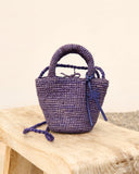 Mini raffia summer bag in purple with braided texture and top handle, styled crossbody over printed linen dress — μικρή καλοκαιρινή τσάντα από ψάθα σε μωβ απόχρωση με πλεκτή υφή και χερούλι, ιδανική για city & resort looks. Διαθέσιμη στο Iconic Angels Glyfada.