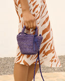 Mini raffia summer bag in purple with braided texture and top handle, styled crossbody over printed linen dress — μικρή καλοκαιρινή τσάντα από ψάθα σε μωβ απόχρωση με πλεκτή υφή και χερούλι, ιδανική για city & resort looks. Διαθέσιμη στο Iconic Angels Glyfada.