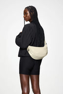 Cream glossy shoulder bag with curved silhouette and adjustable strap, minimalist and versatile, perfect for effortless everyday styling — κρεμ γυαλιστερή shoulder τσάντα με καμπύλη γραμμή και ρυθμιζόμενο λουρί, minimal και ευκολοφόρετη, ιδανική για κομψά daily looks από το πρωί έως το βράδυ. Διαθέσιμη στο Iconic Angels Glyfada.