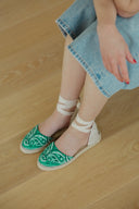 Manebi women’s green bandana espadrilles with flat sole, natural jute base and ankle tie ribbons, combining Mediterranean summer style with relaxed resort elegance for effortless warm-weather outfits — γυναικείες πράσινες espadrilles Manebi με bandana print, φυσική σόλα από jute και κορδέλες που δένουν στον αστράγαλο, ιδανικές για κομψά καλοκαιρινά resort και casual looks. Διαθέσιμες στο Iconic Angels Glyfada.