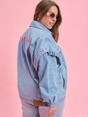 Oversized light blue denim jacket from Project Soma x Barbie collection with pink embroidered Barbie logo and statement streetwear aesthetic — oversized γυναικείο τζιν jacket σε ανοιχτό μπλε από τη συλλογή Project Soma x Barbie, με ροζ κεντημένο Barbie logo και μοντέρνο streetwear χαρακτήρα. Διαθέσιμο στο Iconic Angels Glyfada.