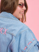 Oversized light blue denim jacket from Project Soma x Barbie collection with pink embroidered Barbie logo and statement streetwear aesthetic — oversized γυναικείο τζιν jacket σε ανοιχτό μπλε από τη συλλογή Project Soma x Barbie, με ροζ κεντημένο Barbie logo και μοντέρνο streetwear χαρακτήρα. Διαθέσιμο στο Iconic Angels Glyfada.