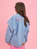 Oversized light blue denim jacket from Project Soma x Barbie collection with pink embroidered Barbie logo and statement streetwear aesthetic — oversized γυναικείο τζιν jacket σε ανοιχτό μπλε από τη συλλογή Project Soma x Barbie, με ροζ κεντημένο Barbie logo και μοντέρνο streetwear χαρακτήρα. Διαθέσιμο στο Iconic Angels Glyfada.