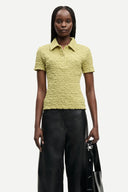 Light olive textured polo top with short sleeves, button placket and fitted silhouette, offering a refined casual feel — λαχανί κοντομάνικο polo top με κουμπιά και ελαστική textured ύφανση, σε εφαρμοστή γραμμή ιδανική για chic casual και modern everyday looks. Διαθέσιμο στο Iconic Angels Glyfada.