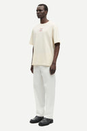 Off-white graphic t-shirt with front and back print details, featuring Samsoe Samsoe leisure lotion artwork in red and blue tones — εκρού κοντομάνικο t-shirt με logo print και summer inspired γραφικά μπροστά και πίσω, σε relaxed γραμμή ιδανική για casual και streetwear looks με playful χαρακτήρα. Διαθέσιμο στο Iconic Angels Glyfada.