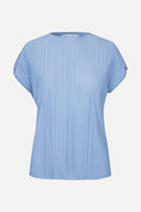 Light blue pleated short sleeve top with fluid silhouette and minimal neckline, offering soft movement and modern elegance — γαλάζιο πλισέ τοπ με κοντό μανίκι και αέρινη γραμμή, ιδανικό για chic casual, office και elevated summer looks με minimal αισθητική. Διαθέσιμο στο Iconic Angels Glyfada.